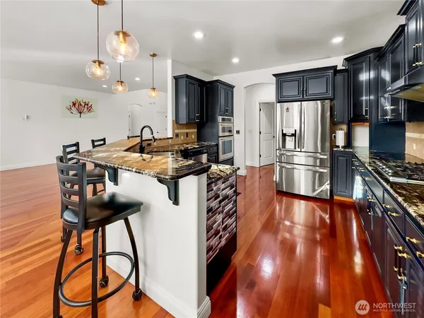 a kitchen with stainless steel appliances a stove a refrigerator a sink dishwasher and a dining table with wooden floor