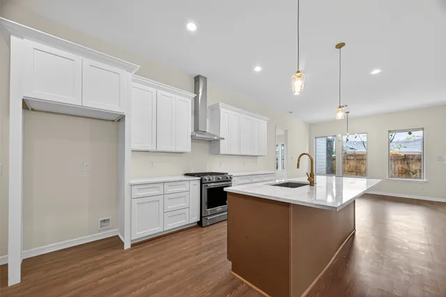a kitchen with stainless steel appliances granite countertop a sink a stove and white cabinets with wooden floor