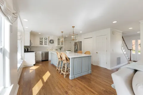 a kitchen with stainless steel appliances kitchen island granite countertop a stove a sink a refrigerator and white cabinets with wooden floor