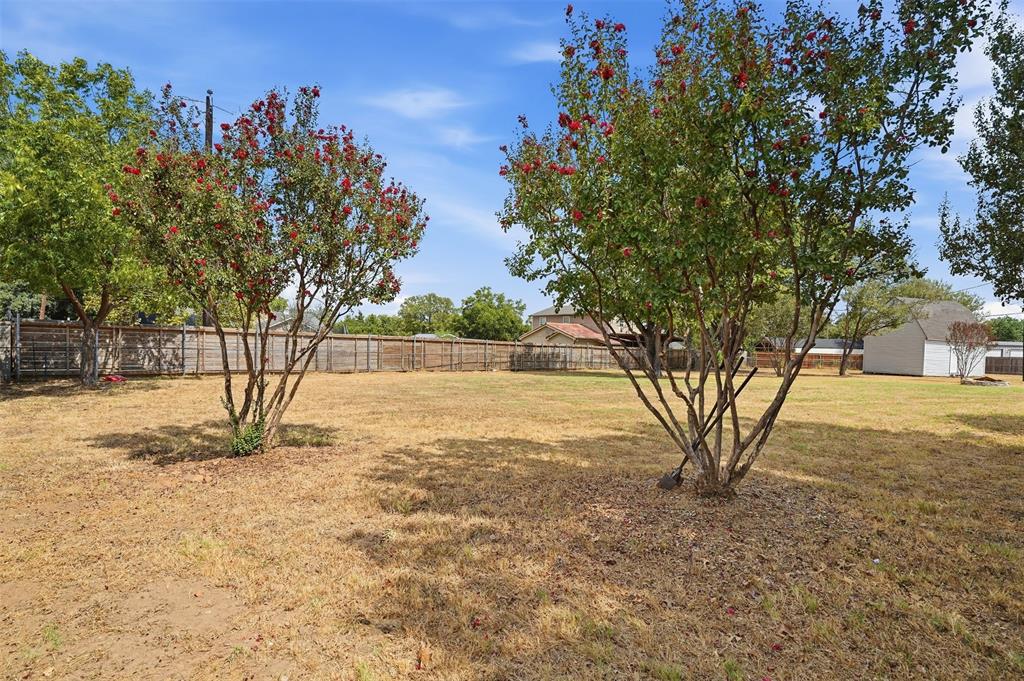 6880 Sandy Beach Road Azle, TX 76020 - Photo 25 of 32 Expansive backyard featuring mature trees with flowering foliage, a wooden privacy fence, and a detached storage shed