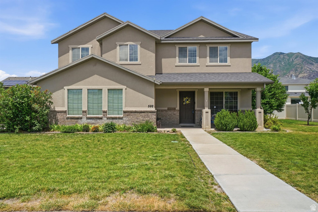 592 West 650 South Springville, UT 84663 - Photo 33 of 33 Two-story stucco and brick exterior featuring a covered front porch, a concrete walkway, and a manicured lawn