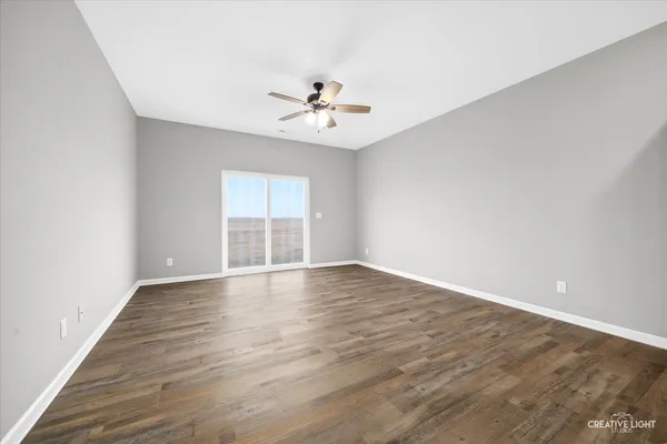 an empty room with wooden floor ceiling fan and windows
