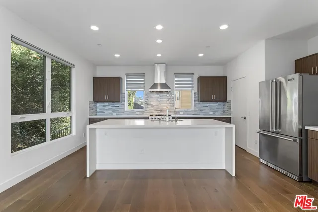 a large kitchen with stainless steel appliances granite countertop a refrigerator a sink dishwasher a stove and a large island with wooden floor