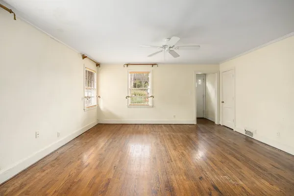 an empty room with wooden floor chandelier fan and windows