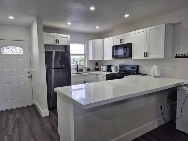 a kitchen with stainless steel appliances granite countertop a refrigerator a sink a stove a microwave and white cabinets with wooden floor