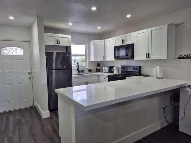 a kitchen with stainless steel appliances granite countertop a refrigerator a sink a stove a microwave and white cabinets with wooden floor