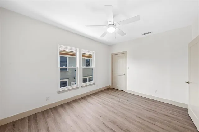 an empty room with wooden floor chandelier fan and windows