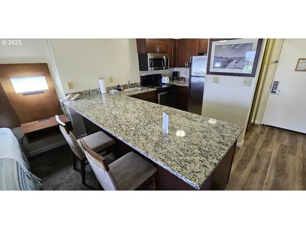 a kitchen view with stainless steel appliances kitchen island granite countertop a refrigerator stove and wooden floor