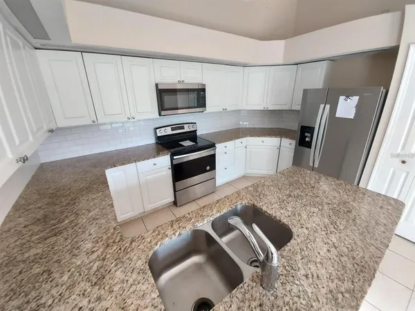 a kitchen with stainless steel appliances granite countertop a sink a stove top oven a refrigerator and white cabinets