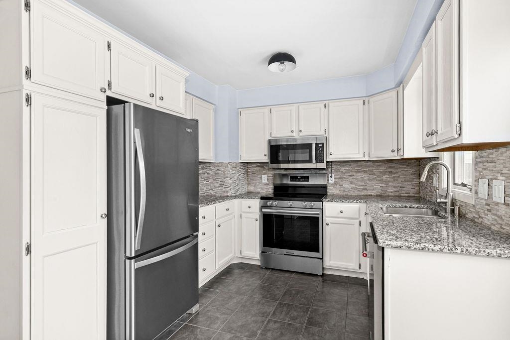 5007 Colorado Street Duluth, MN 55804 - Photo 2 of 31 Kitchen with appliances with stainless steel finishes, light stone counters, white cabinetry, decorative backsplash, and dark tile patterned floors