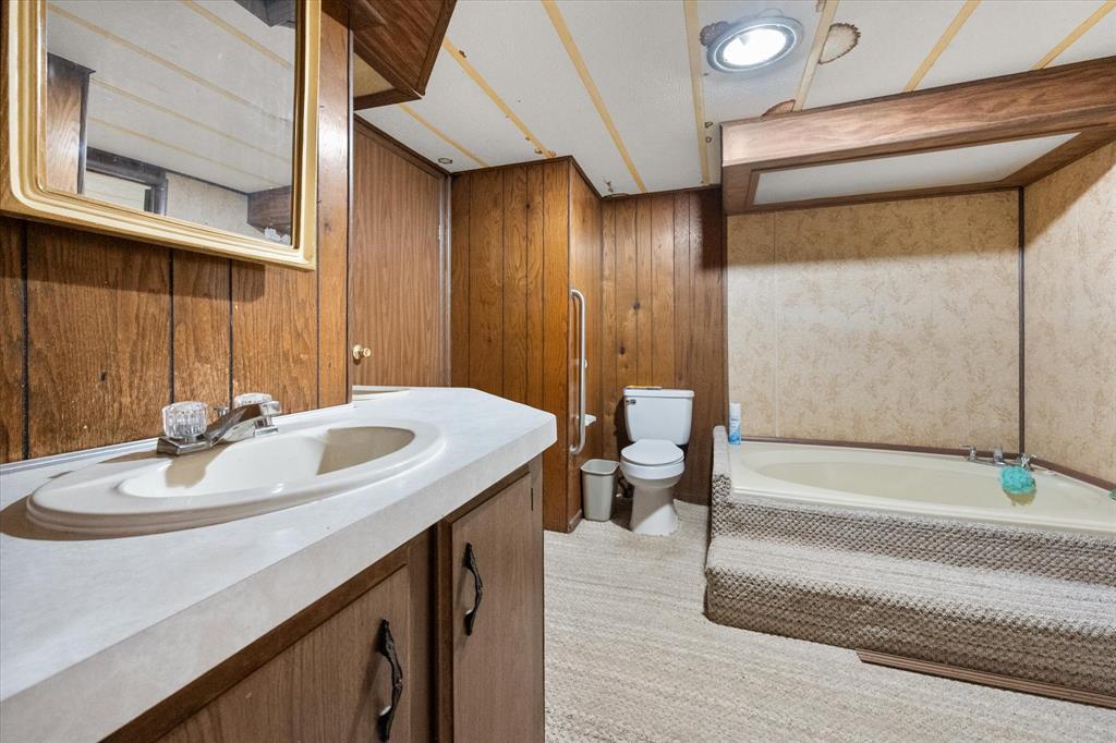 2101 Ridge View Drive Cleburne, TX 76033 - Photo 21 of 31 Bathroom featuring a built-in vanity with an integrated sink, wood-paneled walls, and a recessed bathtub with a textured surround