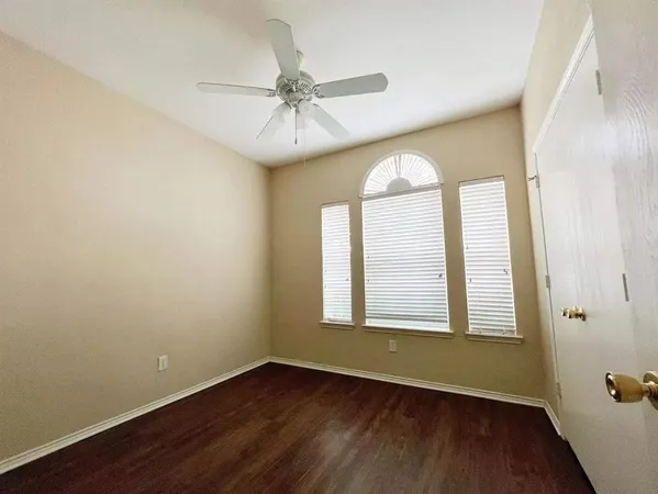 an empty room with wooden floor chandelier fan and windows