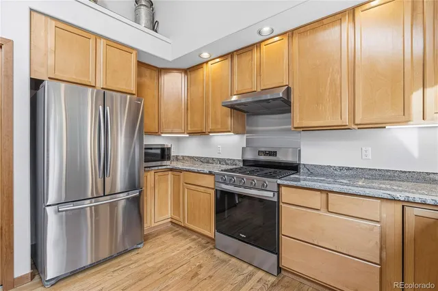 a kitchen with granite countertop stainless steel appliances a refrigerator stove top oven and cabinets
