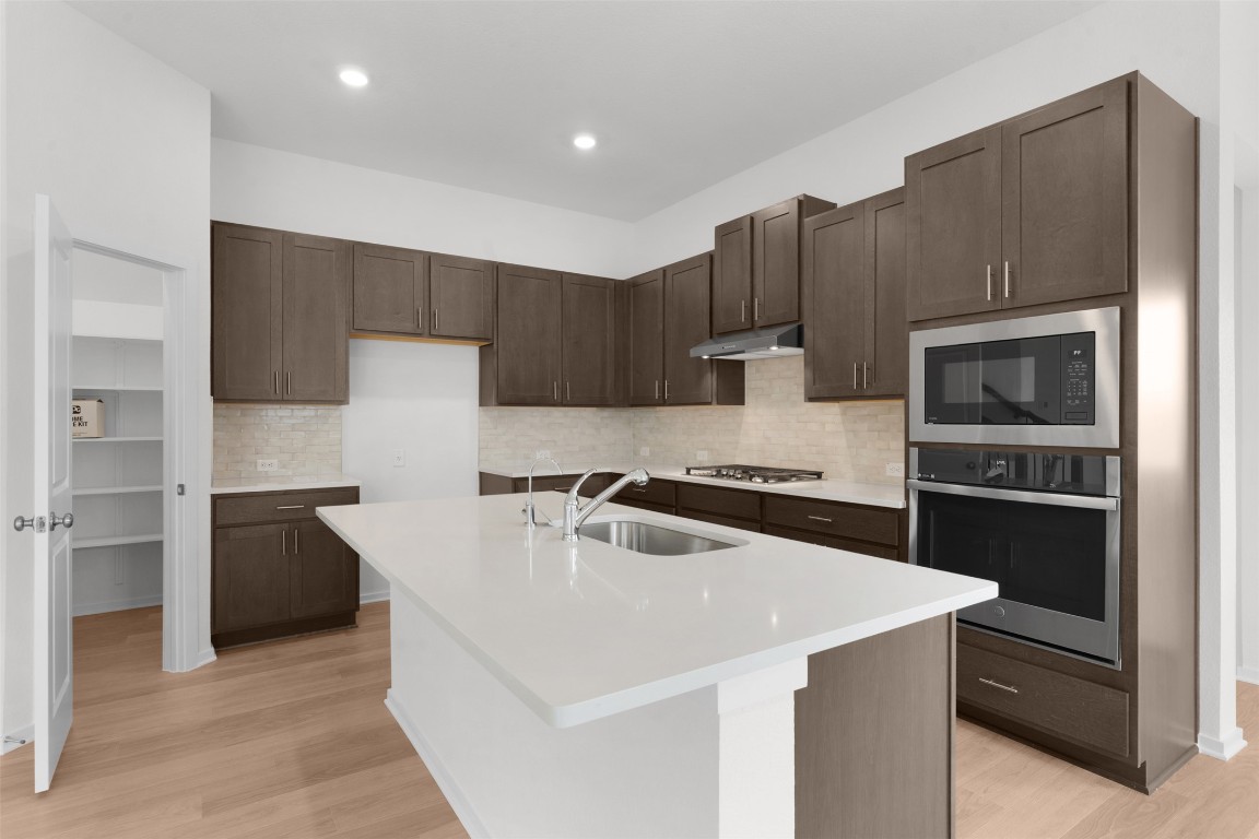 13821 Tucker Hedge Pass Elgin, TX 78621 - Photo 8 of 31 Kitchen with stainless steel appliances, backsplash, a kitchen island with sink, dark brown cabinetry, and light stone countertops