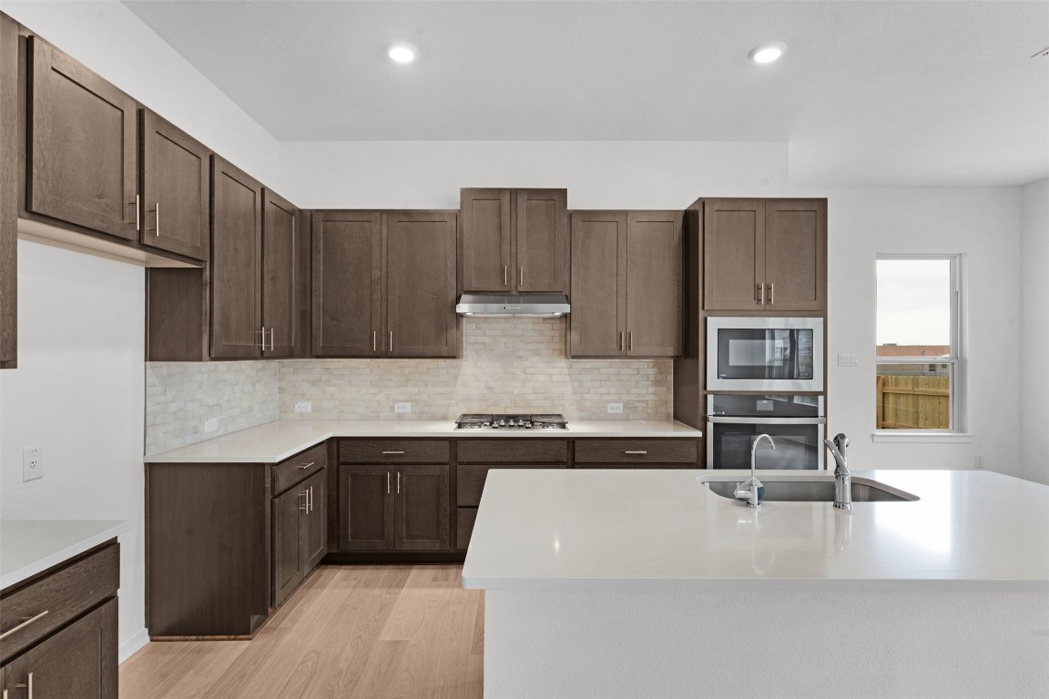 13821 Tucker Hedge Pass Elgin, TX 78621 - Photo 9 of 31 Kitchen with stainless steel appliances, light wood-style floors, light stone counters, tasteful backsplash, and dark brown cabinets