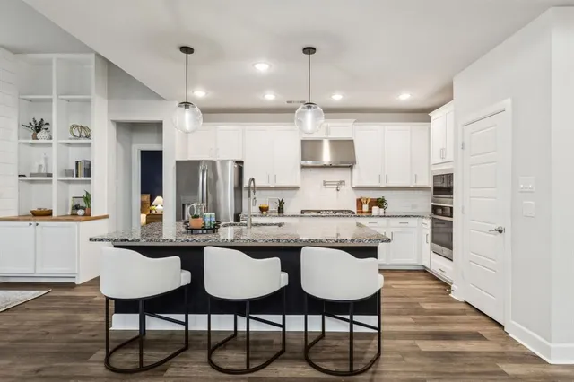 a kitchen with stainless steel appliances kitchen island granite countertop a table chairs refrigerator and microwave