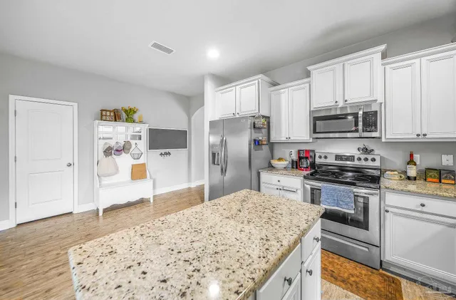 a kitchen with stainless steel appliances kitchen island granite countertop a refrigerator sink and white cabinets