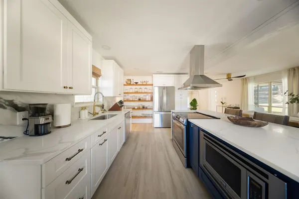 a kitchen with stainless steel appliances a sink dishwasher stove and white cabinets with wooden floor