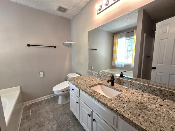 a bathroom with a granite countertop sink a large mirror a toilet and a window