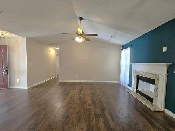 a view of an empty room with wooden floor fireplace and a window