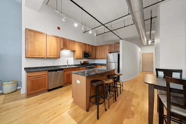 a kitchen with stainless steel appliances granite countertop a sink a stove a refrigerator cabinets and chairs