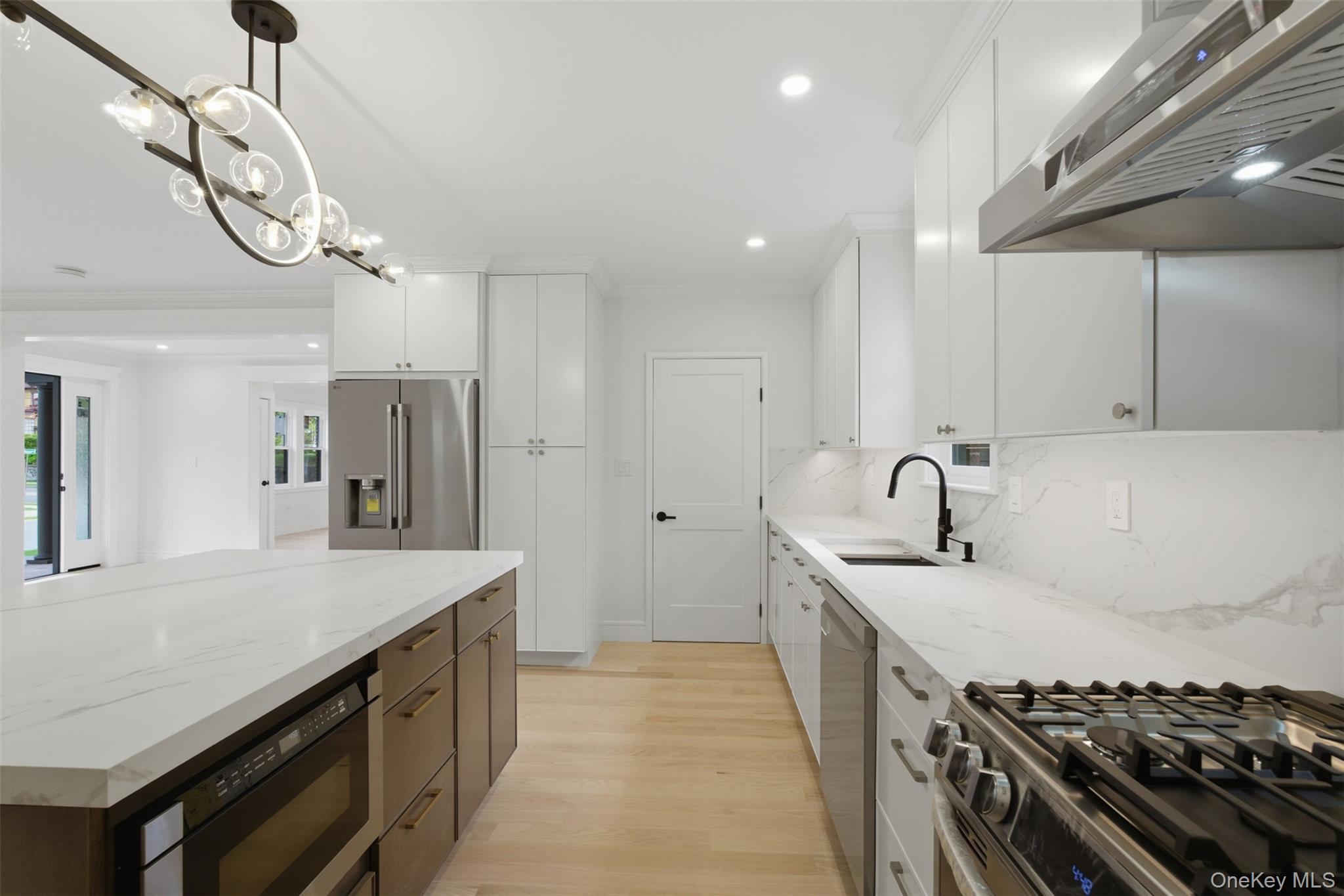 40 Calhoun Avenue New Rochelle, NY 10801 - Photo 7 of 49 Contemporary kitchen featuring an expansive center island with built-in microwave, white shaker cabinetry, stainless steel appliances, and wood-finish flooring
