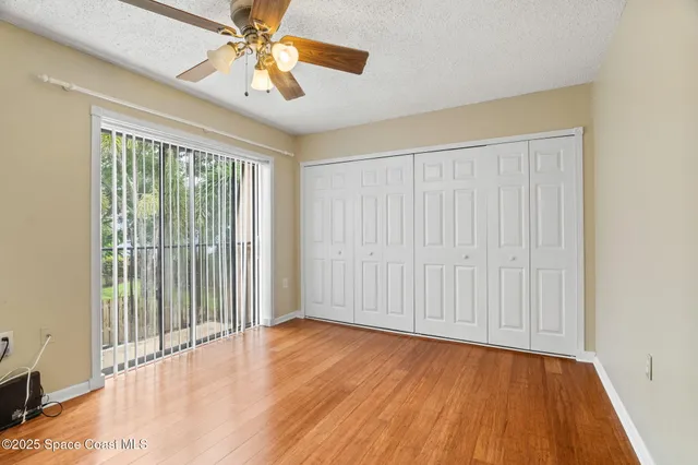 an empty room with wooden floor chandelier fan and windows