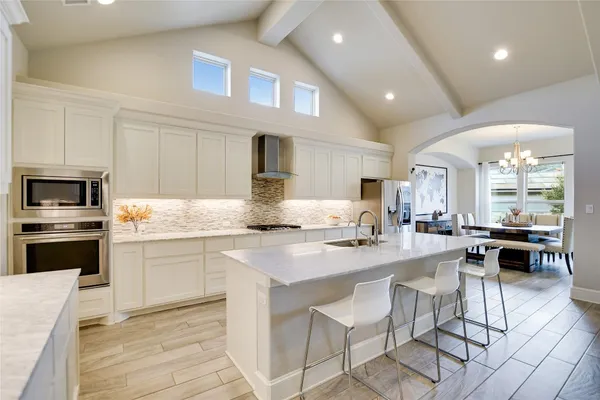 a kitchen with stainless steel appliances granite countertop a stove top oven a sink dishwasher a dining table and chairs with wooden floor