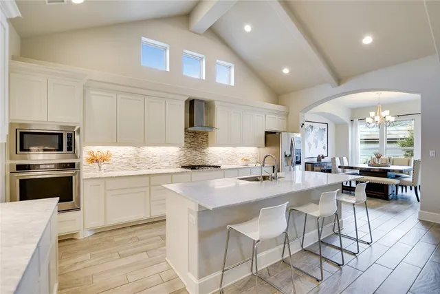 a kitchen with stainless steel appliances granite countertop a stove top oven a sink dishwasher a dining table and chairs with wooden floor