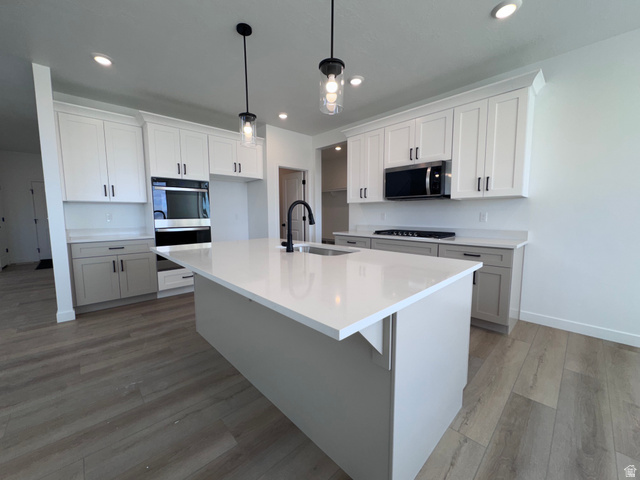 2633 Scarlet Road, Unit 259 Eagle Mountain, UT 84005 - Photo 8 of 30 Modern kitchen featuring a large central island with a sink and matte black faucet, light-toned countertops, and two-tone cabinetry with black hardware