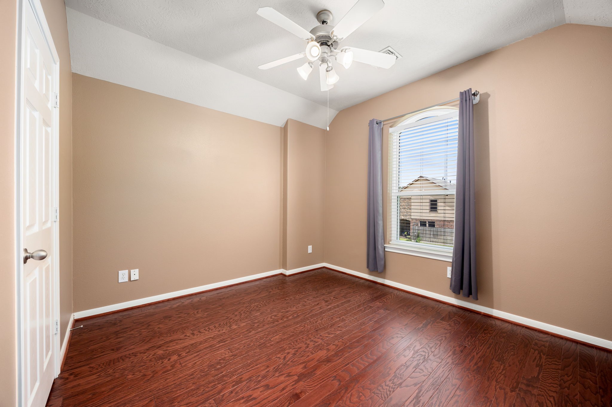 4526 Countrypines Drive Spring, TX 77388 - Photo 27 of 38 Generously sized secondary bedroom featuring rich wood-look flooring and a unique sloped ceiling accent. The room comes equipped with a modern ceiling fan, media-ready wall outlets, and a large arched window that lets in ample natural light.