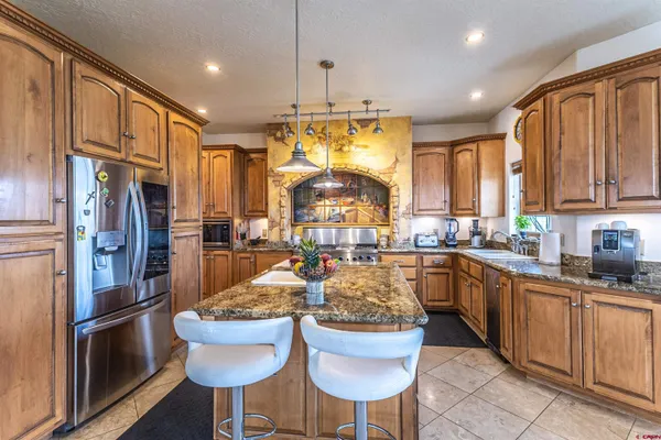 a kitchen with stainless steel appliances granite countertop a refrigerator a sink dishwasher a dining table and chairs with wooden floor