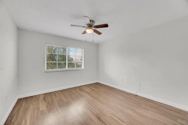 an empty room with wooden floor ceiling fan and windows