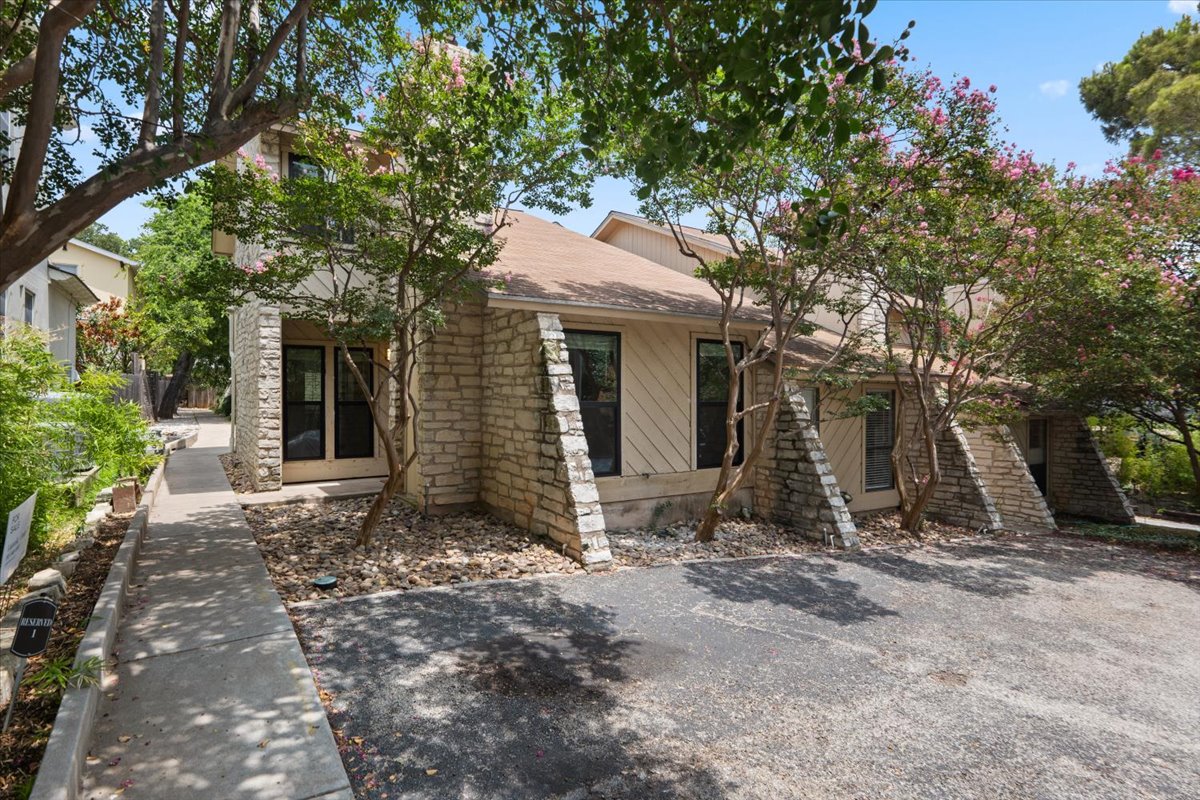 2500 Enfield Road, Unit 1 Austin, TX 78703 - Photo 2 of 26 A stone-accented facade complements mature trees and a paved driveway, offering a charming entrance.