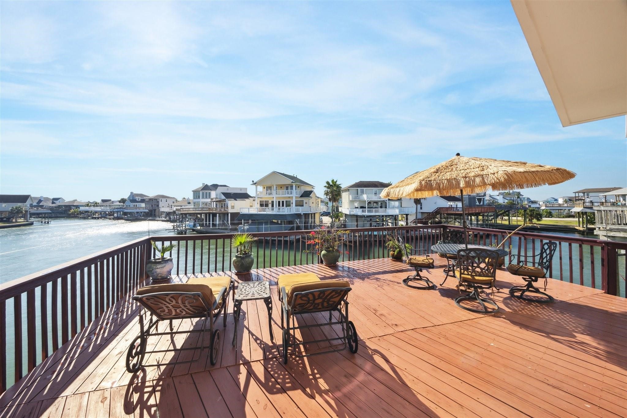 410 Isles End Road Tiki Island, TX 77554 - Photo 12 of 13 Spacious waterfront deck with stunning canal views, featuring patio furniture and a large umbrella, perfect for outdoor relaxation and entertaining.