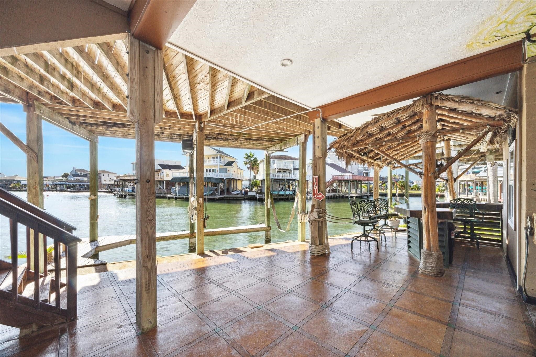 410 Isles End Road Tiki Island, TX 77554 - Photo 13 of 13 This waterfront patio offers a spacious, covered outdoor area with a thatched-roof section, perfect for relaxing and entertaining. It provides scenic views of the canal and ideal for those who love waterfront living.