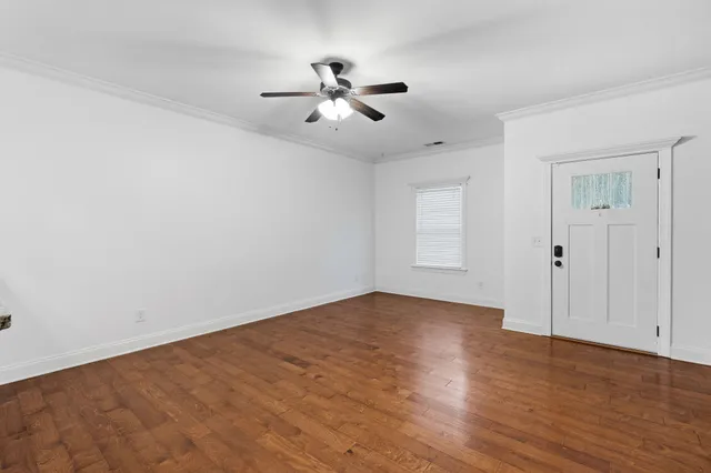 an empty room with wooden floor fan and windows