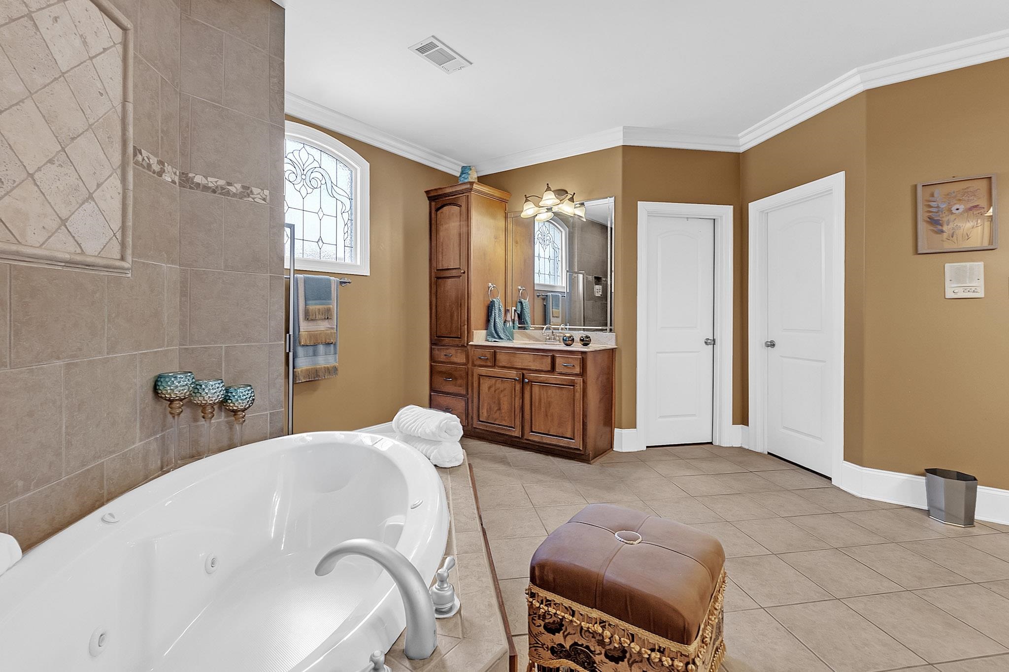 649 Ridge Springs Road Collierville, TN 38017 - Photo 25 of 38 Spacious bathroom featuring a white soaking tub with integrated jets, a wood-finish vanity with an integrated sink, and an arched decorative window