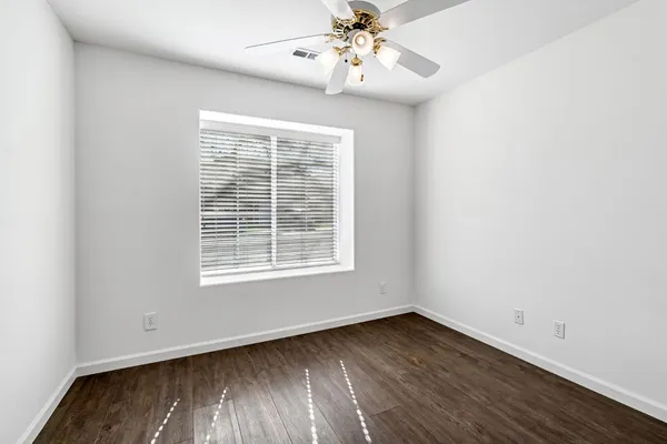 an empty room with wooden floor fan and windows