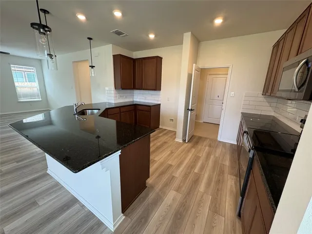 a kitchen with stainless steel appliances granite countertop a refrigerator a stove and a sink with wooden floor