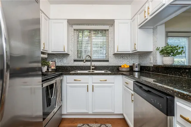 a kitchen with stainless steel appliances granite countertop a sink dishwasher a stove and a refrigerator with wooden floor