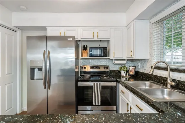 a kitchen with stainless steel appliances granite countertop a sink a stove a refrigerator a washer dryer and cabinets