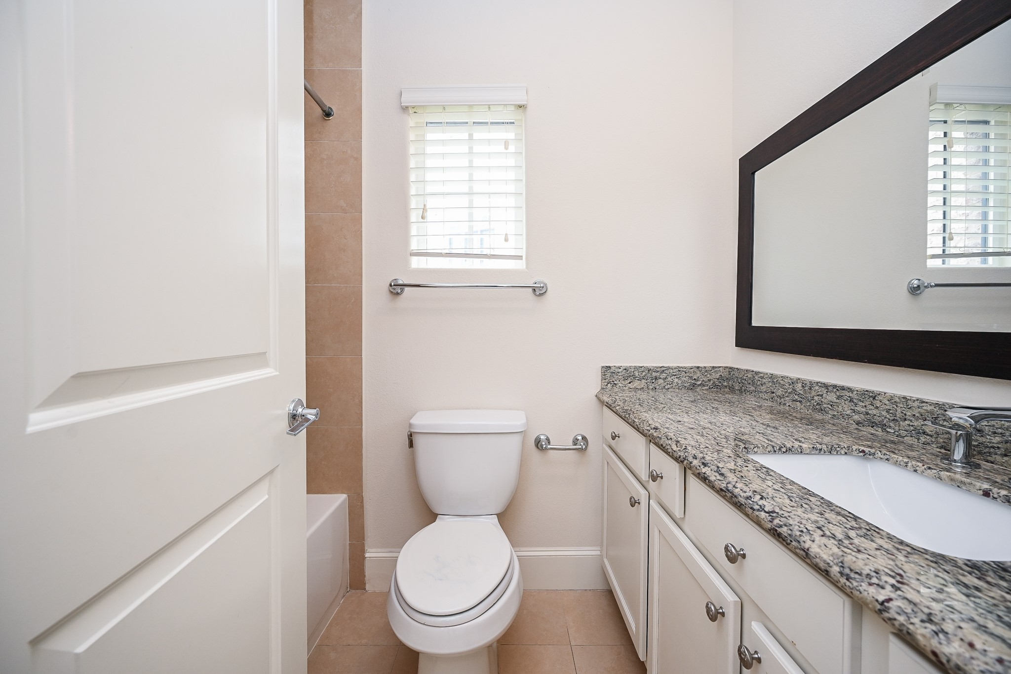 9546 London Bridge Station Houston, TX 77045 - Photo 25 of 41 Discover luxury in this ensuite bathroom with a granite-topped single sink, expansive framed mirror, ample cabinet storage, and a breezy window enhancing the inviting shower-tub combo.