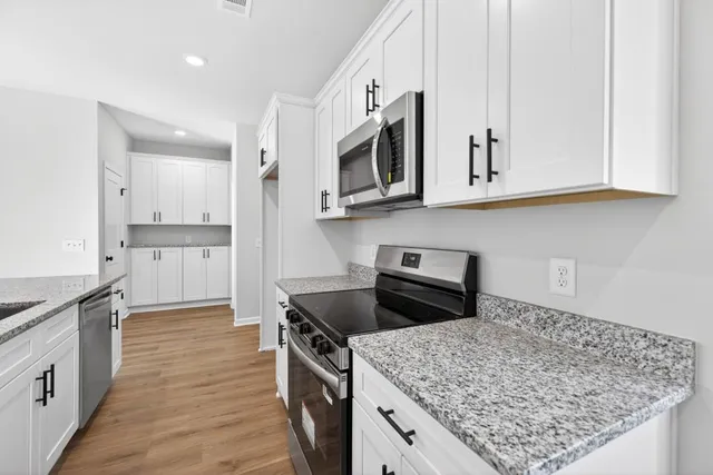 a open kitchen with stainless steel appliances granite countertop a sink dishwasher and white cabinets with wooden floor
