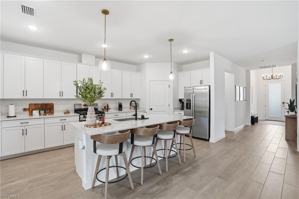20428 Verawood Loop Estero, FL 33928 - Photo 8 of 50 Kitchen featuring stainless steel appliances, a breakfast bar, decorative light fixtures, light wood-style flooring, and an island with sink