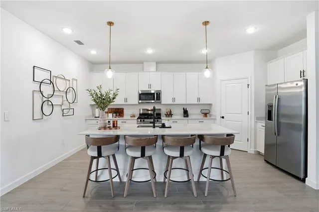 a kitchen with stainless steel appliances kitchen island granite countertop a dining table chairs refrigerator and microwave