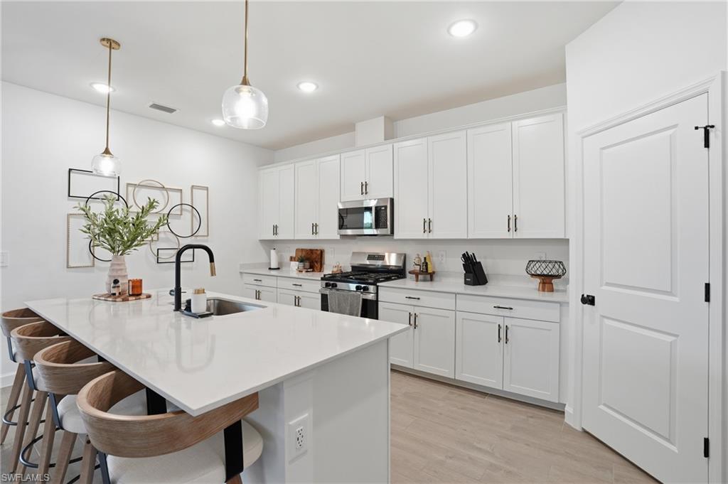 20428 Verawood Loop Estero, FL 33928 - Photo 10 of 50 Kitchen featuring appliances with stainless steel finishes, pendant lighting, white cabinetry, a breakfast bar, and light wood-style flooring