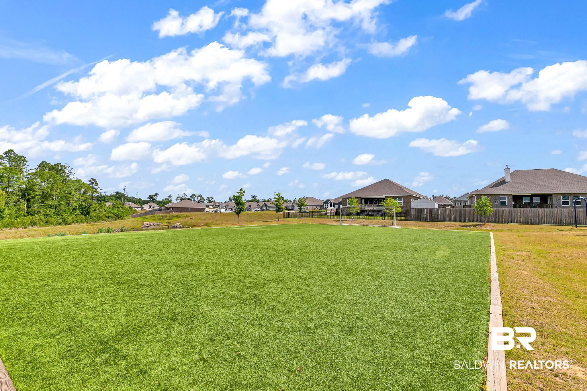 13233 Ibis Boulevard Daphne, AL 36527 - Photo 89 of 100 Expansive recreational green space with a manicured lawn, visible goalposts, and perimeter fencing, surrounded by mature trees and residential properties