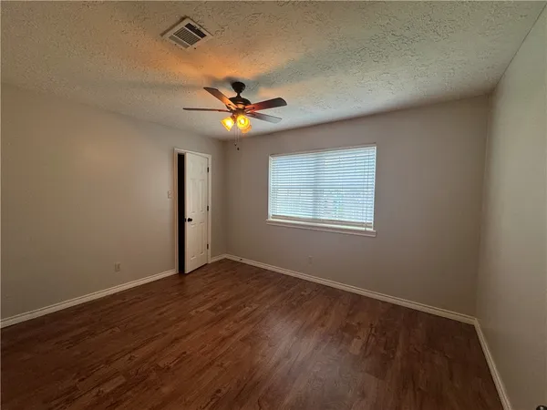 an empty room with wooden floor fan and windows