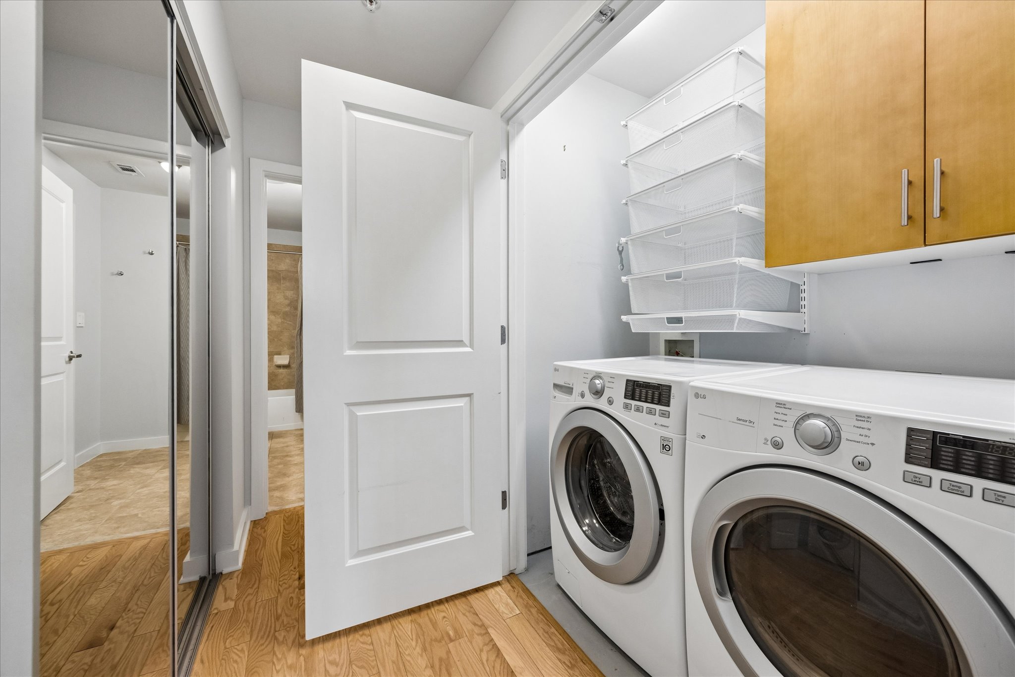 360 Nueces Street, Unit 2005 Austin, TX 78701 - Photo 16 of 35 Dedicated laundry area featuring a front-loading washer and dryer, wall-mounted storage baskets, and overhead cabinetry